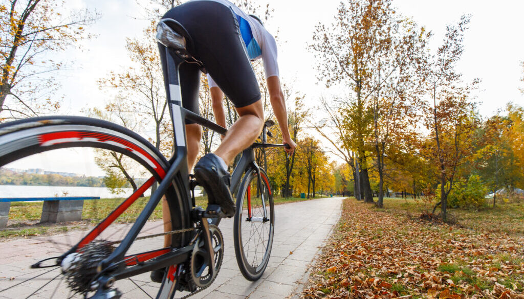 Young male triathlete riding bike in autumn park